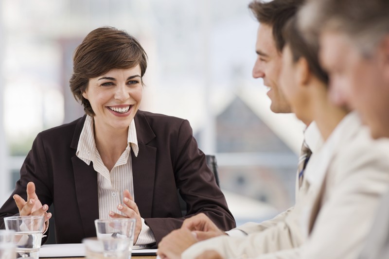 Happy businesswoman discussing with colleagues at meeting in office
